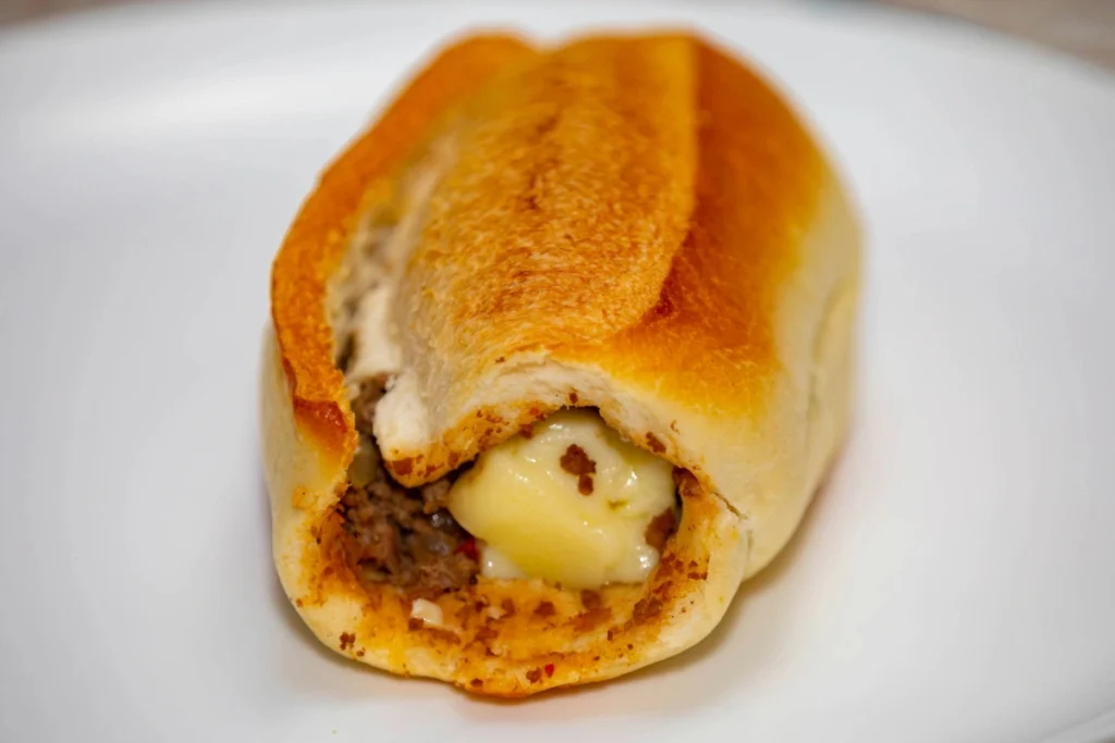  Close-up de um pão francês sem miolo, preenchido generosamente com carne moída bem temperada e uma camada central de queijo muçarela derretido e cremoso, uma receita conhecida como buraco quente.