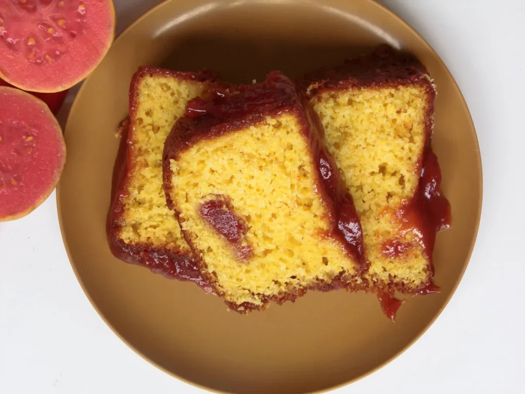 Vista superior de fatias de bolo de fubá com goiabada, ao lado de uma goiaba cortada.