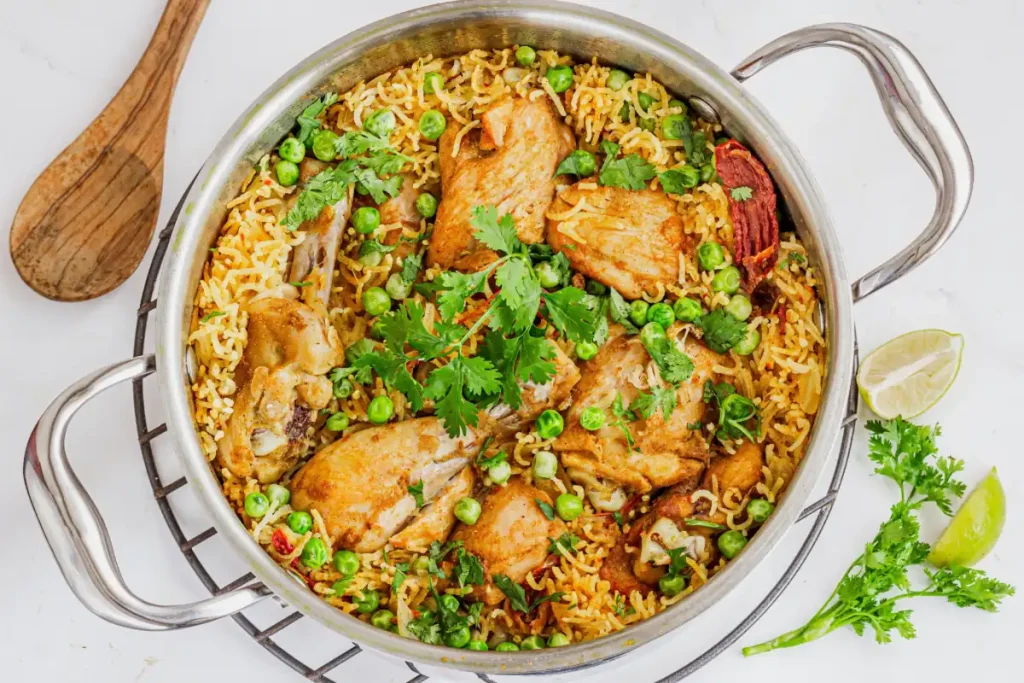 Panela com galinhada, destacando ingredientes como o cheiro verde, ervilha, frango, arroz e limão.