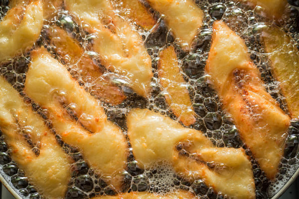 Tiras de massa sendo fritas em óleo quente para preparar cueca virada, doce tradicional brasileiro, até ficarem douradas e crocantes. 