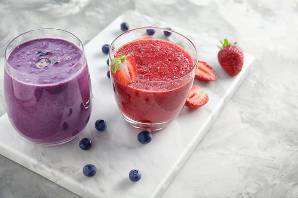 Copos com diferentes smoothies sobre uma placa de pedra, incluindo opções de frutas como mirtilo e morango.