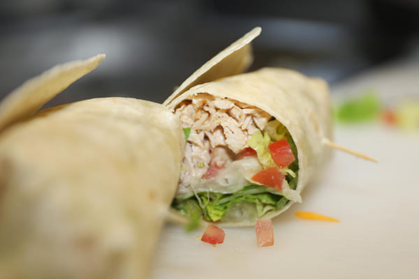 Close-up de um wrap recheado com frango desfiado, vegetais frescos e molho, servido em um prato.