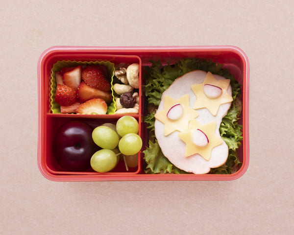 Lancheira escolar saudável em estilo bento, com sanduíche decorado e morangos frescos organizados em compartimentos.