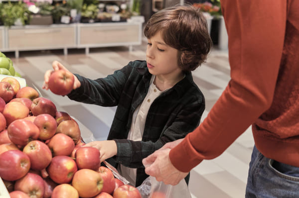 Pai e filho escolhendo maçãs juntos, destacando a importância de hábitos alimentares saudáveis, em um momento alegre e educativo.