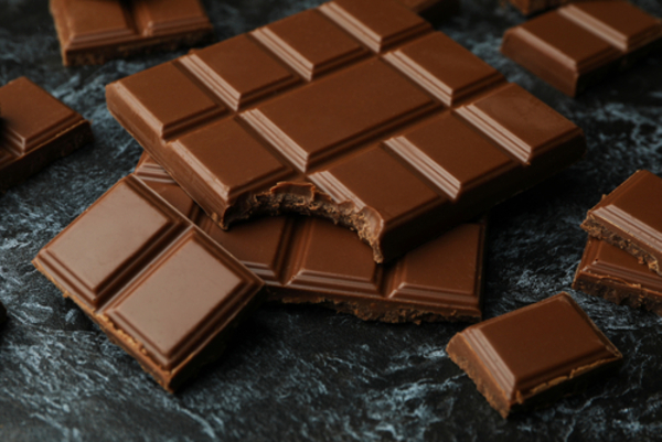 Saiba quais são os 11 alimentos proibidos para cães e gatos 4 Barras de chocolate apetitosas dispostas sobre uma superfície preta esfumaçada, com pedaços quebrados revelando o interior cremoso.