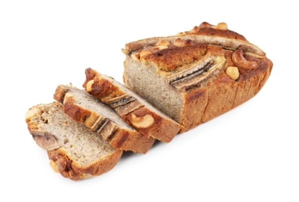 Bolo de banana vegano: receita fácil, saudável e deliciosa  1 Bolo de banana caseiro cortado em fatias, com pedaços de noz ao lado, sobre fundo branco.