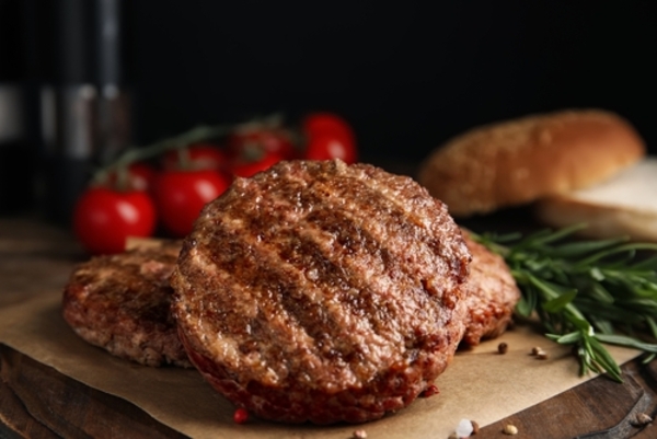 Hambúrguer caseiro: 4 receitas para impressionar  1 Hambúrgueres grelhados e suculentos sobre uma tábua de madeira, acompanhados de temperos e ingredientes frescos ao redor.