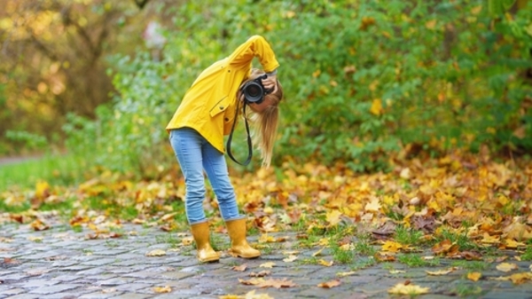 Top 18 ideias de presentes criativos para um Dia das Crianças inesquecível 4 Menina usando galochas amarelas e casaco combinando, segurando uma câmera fotográfica em meio a folhas caídas, capturando imagens em um ambiente natural de outono.