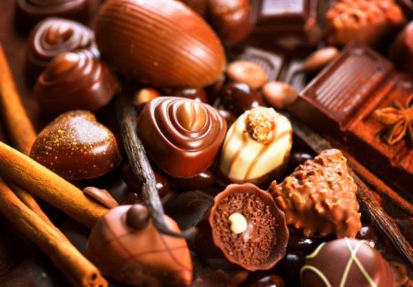Presentes para o Dia dos Professores: 7 ideias cheias de carinho para surpreender 2 Variedade de bombons e chocolates artesanais em diferentes formatos e texturas, incluindo coberturas com nozes, confeitos e drizzles decorativos. Há chocolates escuros, ao leite e brancos, acompanhados por paus de canela e favas de baunilha.