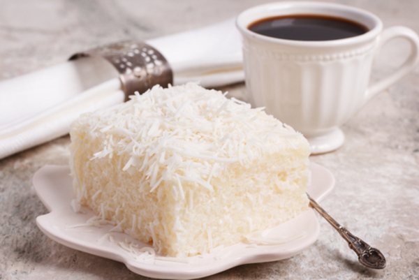 Bolo de tapioca brasileiro servido em uma travessa, com textura granulada e cobertura de coco ralado, típico das festas juninas e sobremesas regionais. 