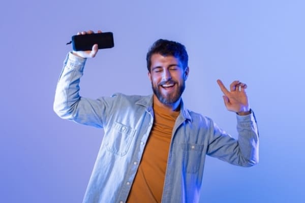 12 ideias de presentes de Natal para homens que nunca falham 8 Homem jovem com barba, usando jaqueta jeans casual, posando com expressão confiante contra fundo neutro.