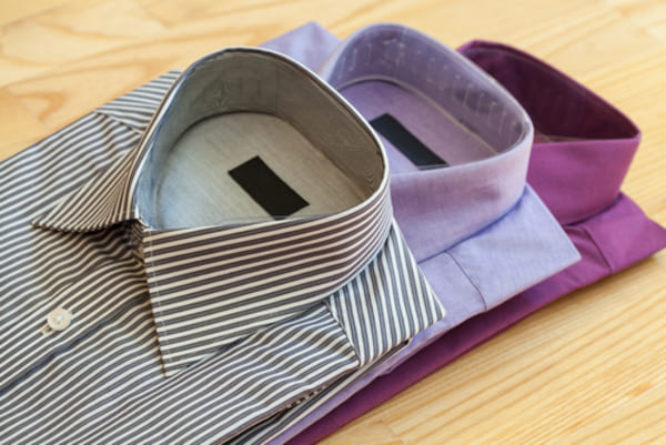 12 ideias de presentes de Natal para homens que nunca falham 1 Conjunto de camisas masculinas estilosas feitas de algodão, penduradas em cabides, exibindo diferentes cores e padrões sobre um fundo neutro.