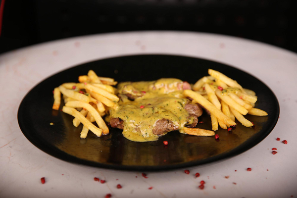  Vista superior de um prato com bife grelhado ao molho de mostarda, acompanhado de batatas fritas, sobre uma mesa. 