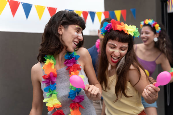 Vai passar o carnaval em casa? Confira 8 ideias criativas para curtir a folia sem sair do lar 1 Pessoas comemorando o carnaval em casa, usando fantasias coloridas e sorrindo enquanto se divertem em um ambiente festivo e decorado com bandeiras coloridas.