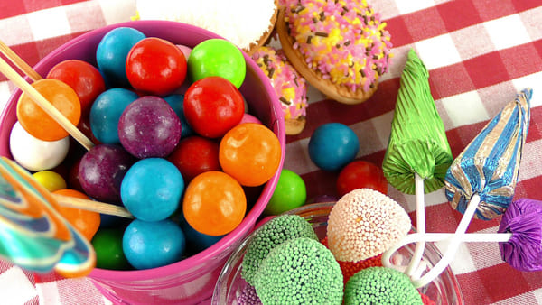 Vai passar o carnaval em casa? Confira 8 ideias criativas para curtir a folia sem sair do lar 2 Vista superior de uma mesa com doces multicoloridos, lembrando guloseimas típicas de festas de Carnaval, dispostos de forma vibrante e atrativa.