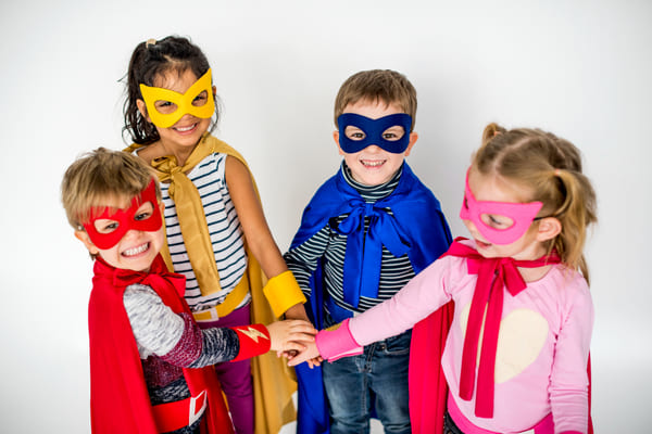 Vai passar o carnaval em casa? Confira 8 ideias criativas para curtir a folia sem sair do lar 3 Crianças brincando fantasiadas de super-heróis, sorrindo e se divertindo em um ambiente interno iluminado.