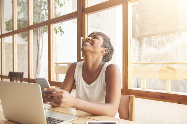 Jovem mulher morena sentada em um café iluminado pela luz natural, usando laptop sobre a mesa enquanto aproveita a claridade do dia. 