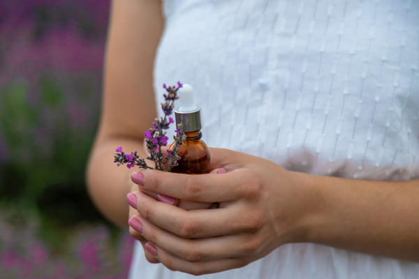Como limpar energia da casa? Técnicas de limpeza para renovar seu lar 6 Mulher em campo de lavanda segurando uma pequena garrafa de óleo essencial natural, com foco seletivo nas flores roxas ao redor, transmitindo sensação de bem-estar e conexão com a natureza.