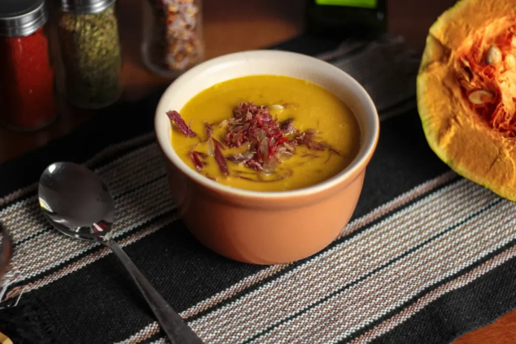 Tigela de caldo de abóbora cremoso finalizado com carne seca desfiada e cebola, uma receita de outono.