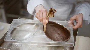 Confeiteiro preenchendo forma de ovo de Páscoa com chocolate derretido.