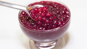 Close-up de uma colher de prata levantando sagu com suco de uva, de cor púrpura vibrante.