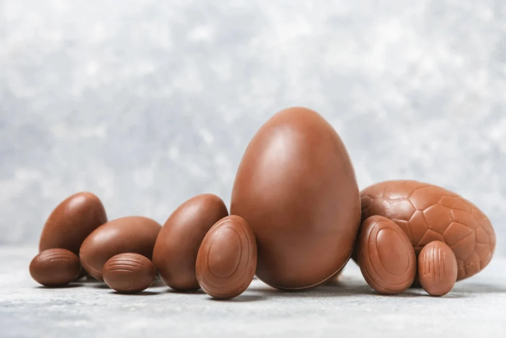 Composição linear com ovos de Páscoa de chocolate ao leite, variando de mini ovinhos a ovos grandes, com acabamento liso e brilhante.