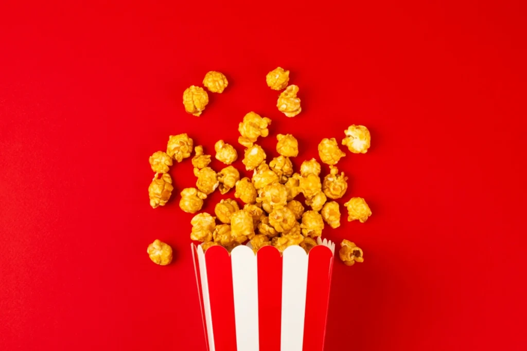 Pipoca doce em embalagem vermelha e branca, espalhada sobre fundo vermelho.