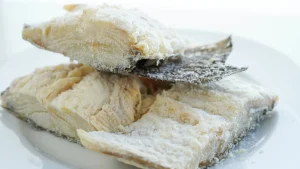 Três postas de bacalhau com pele sobre prato branco.