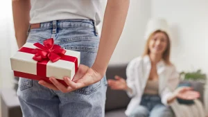 Pessoa escondendo presente de Dia das Mães com laço vermelho atrás das costas, pronto para entregar para a mãe.
