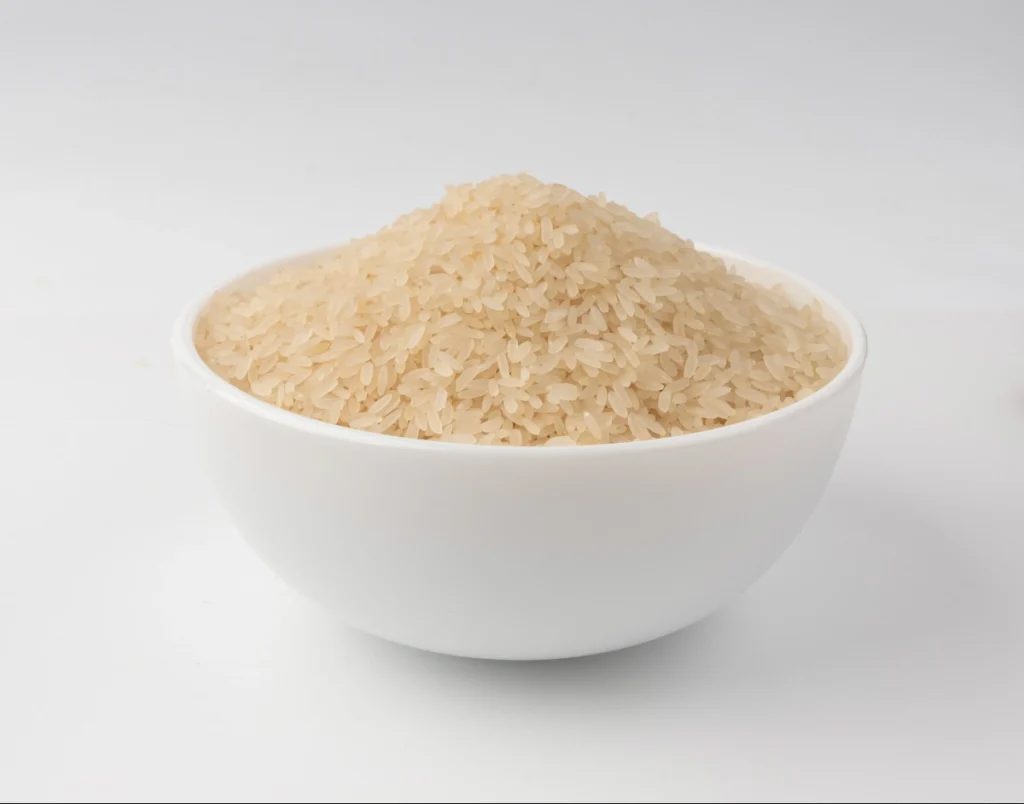 Uma tigela branca redonda e cheia de arroz parboilizado cru, centralizada contra um fundo branco e limpo.