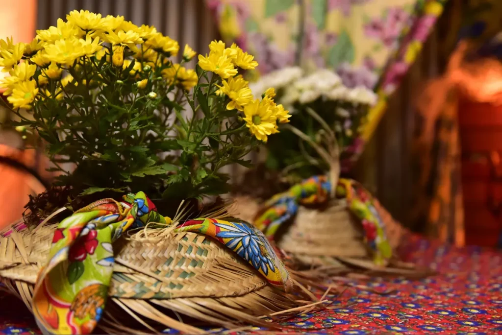  Mesa decorada para a festa junina, com tecido chita, flores e chapéus de palha.